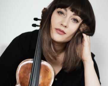 Kobieta z brązowymi włosami i grzywką. O twarz opiera skrzypce. Lewą ręką dotyka twarzy.